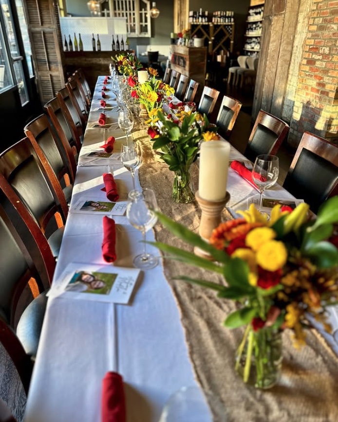 A long private dining table at Falcon & Fig set with flowers, candles, glassware, and red napkins